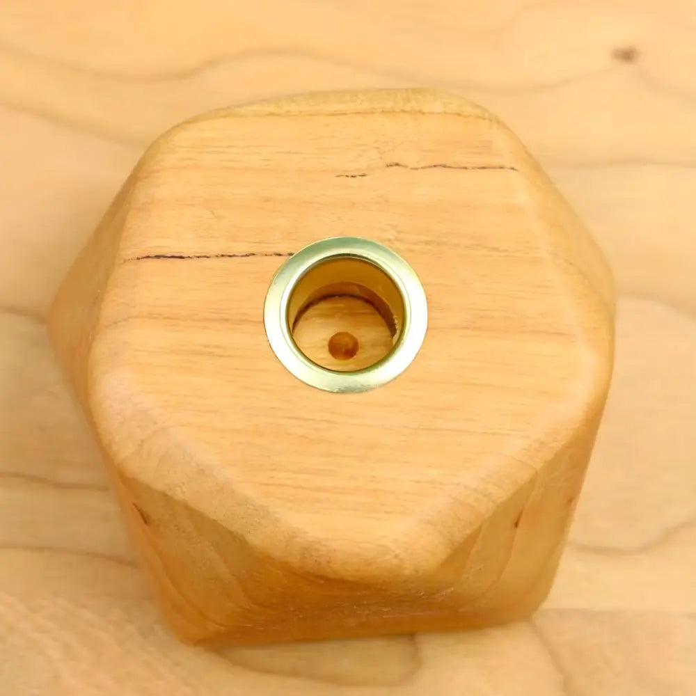 Wooden hexagonal candle holder with a brass fitting on a wooden surface