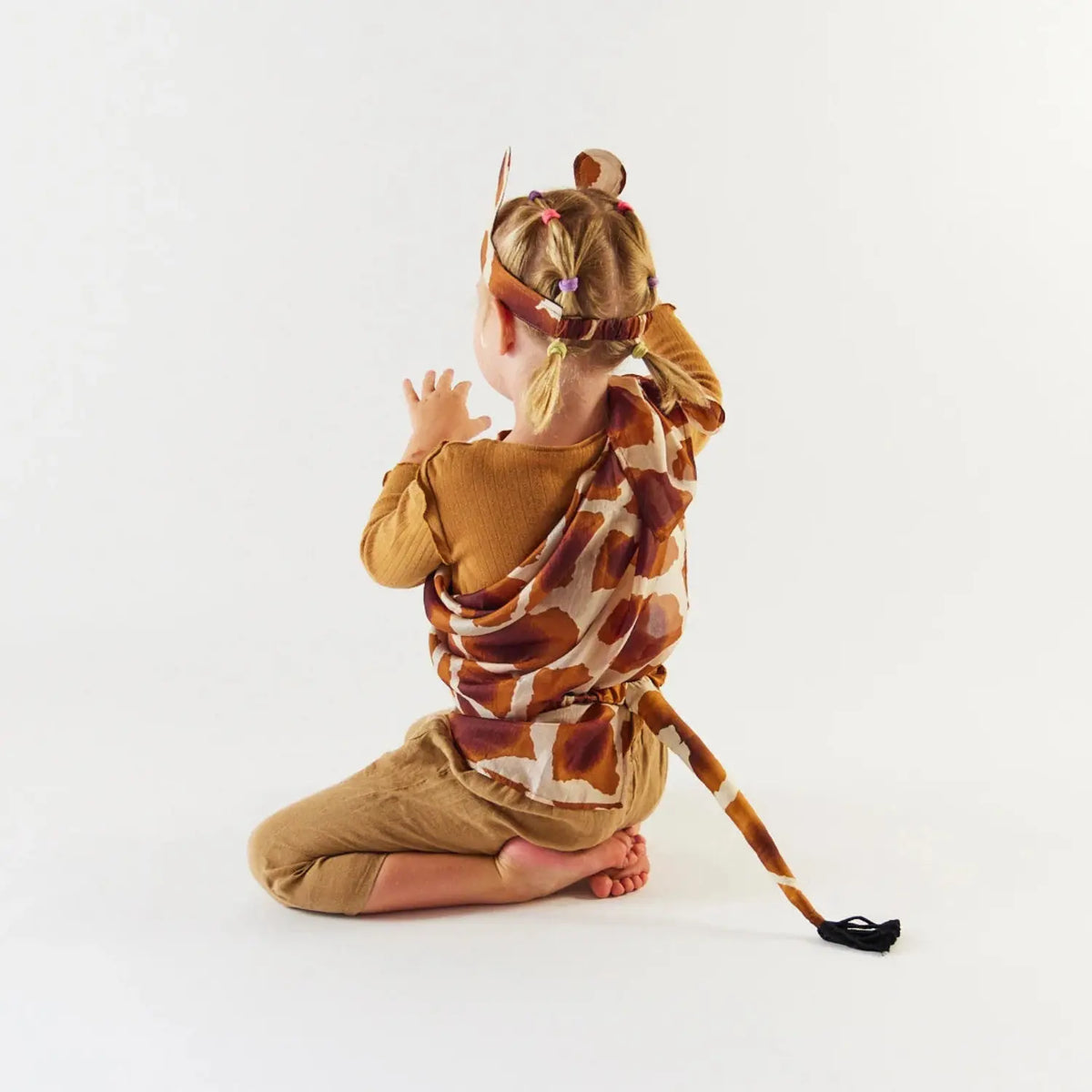 Back view of a kneeling child wearing a giraffe Playsilk with silk giraffe ears and a tail