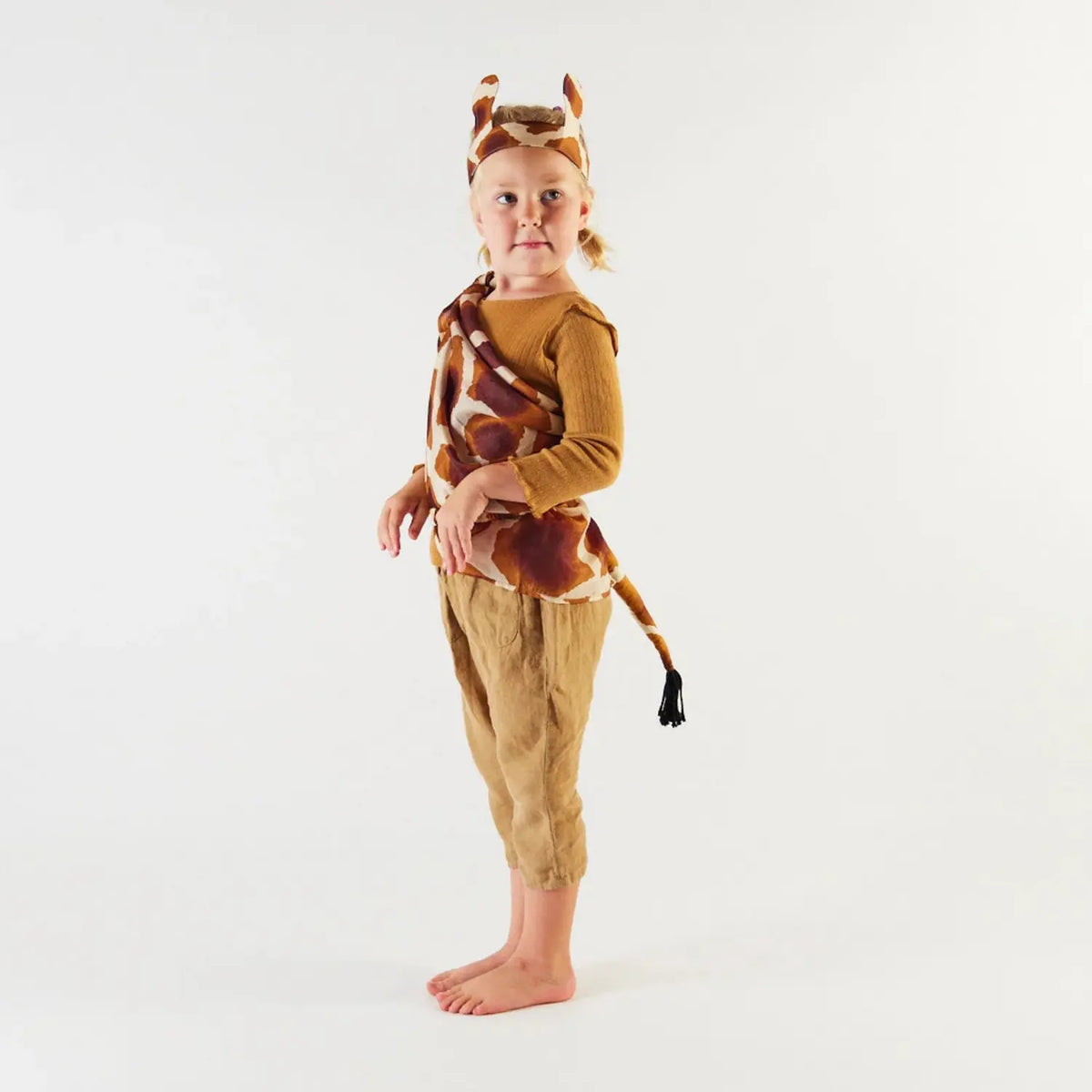 Side view of a child wearing silk giraffe ears and a giraffe playsilk for imaginative animal play