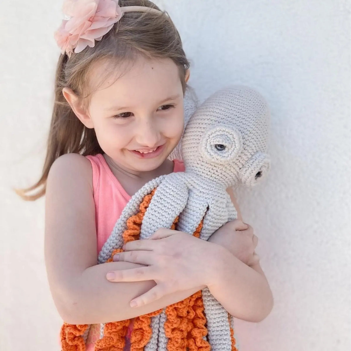 Smiling child hugging a light gray crochet octopus soft toy, its orange-ruffled arms hanging down