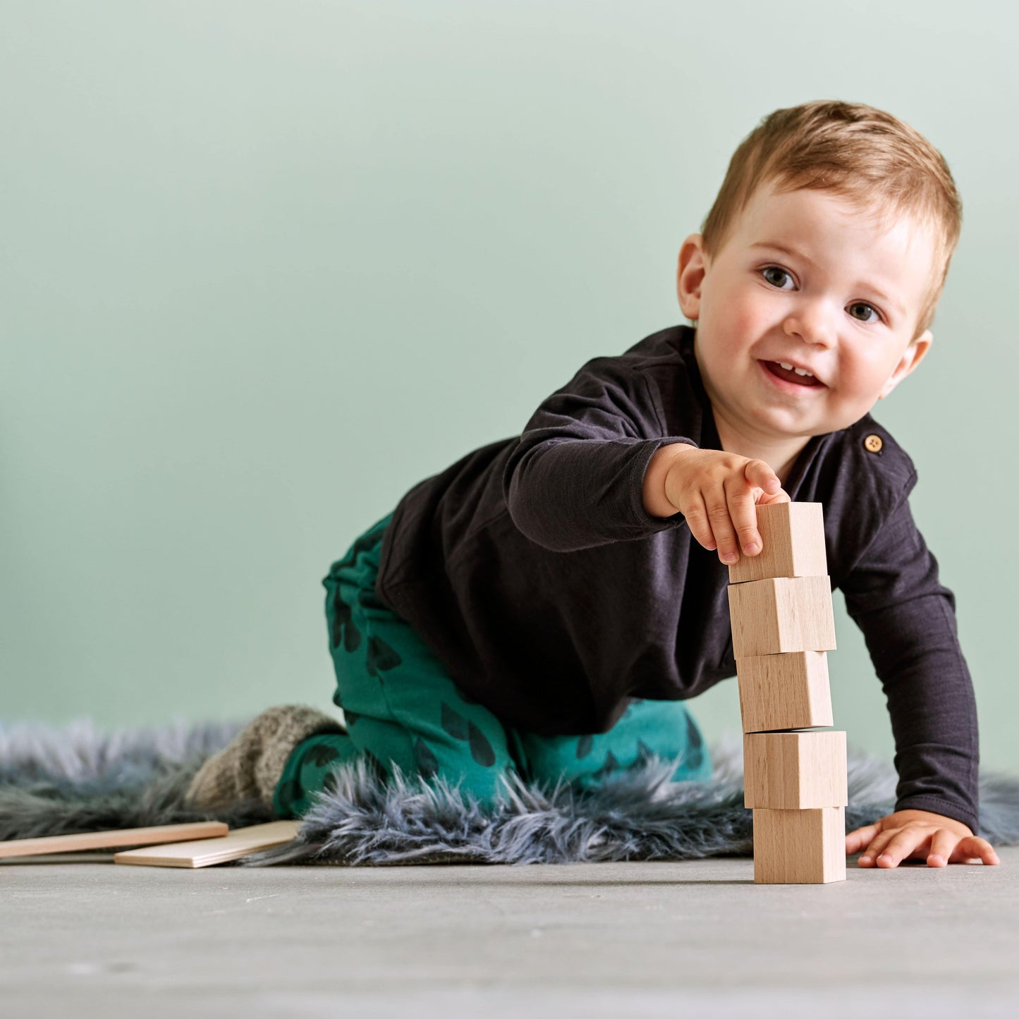 Child lying on floor stacking wooden building blocks in imaginative play