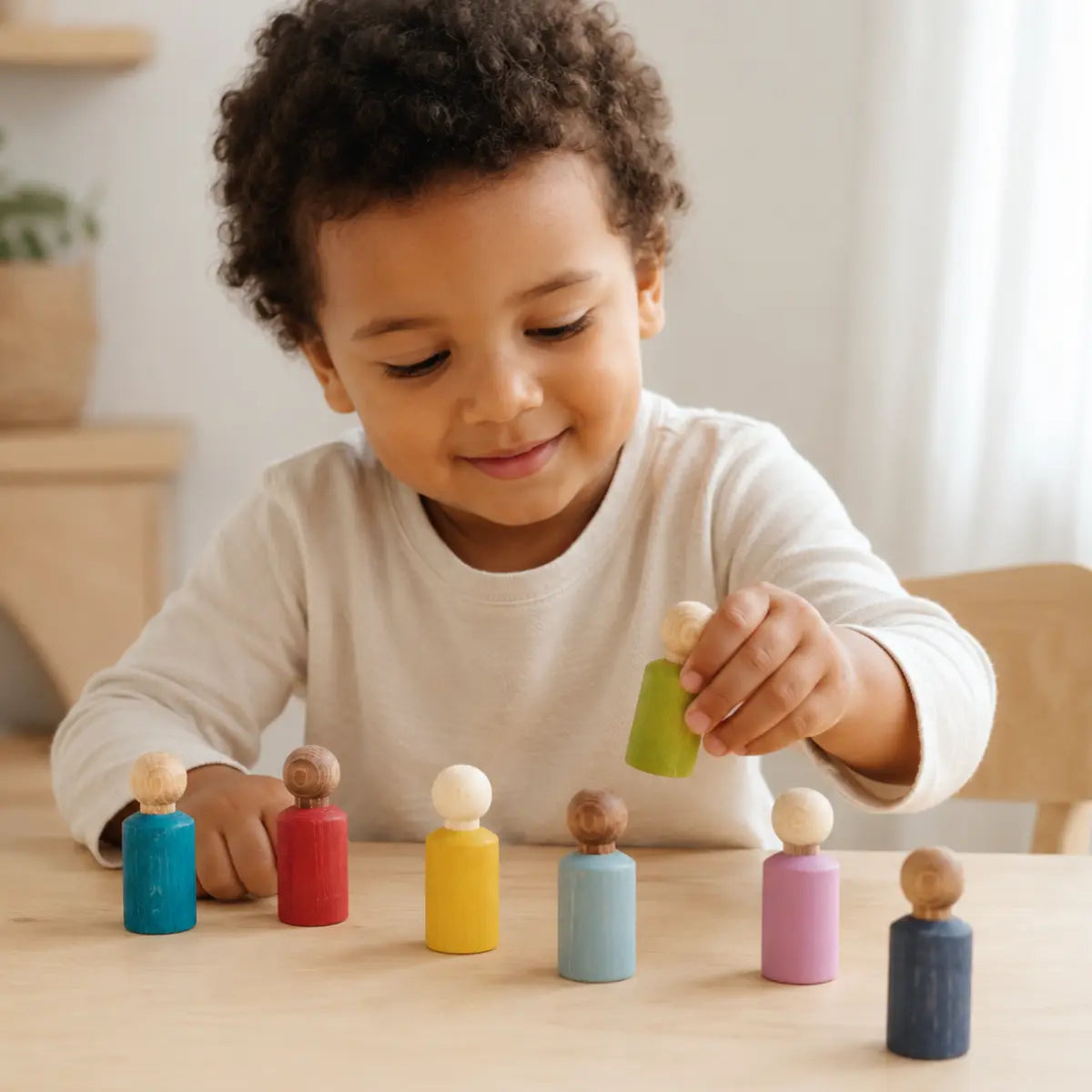 Child playing with seven Lubulona My Buddies wooden peg dolls in assorted colors for small world and imaginative play