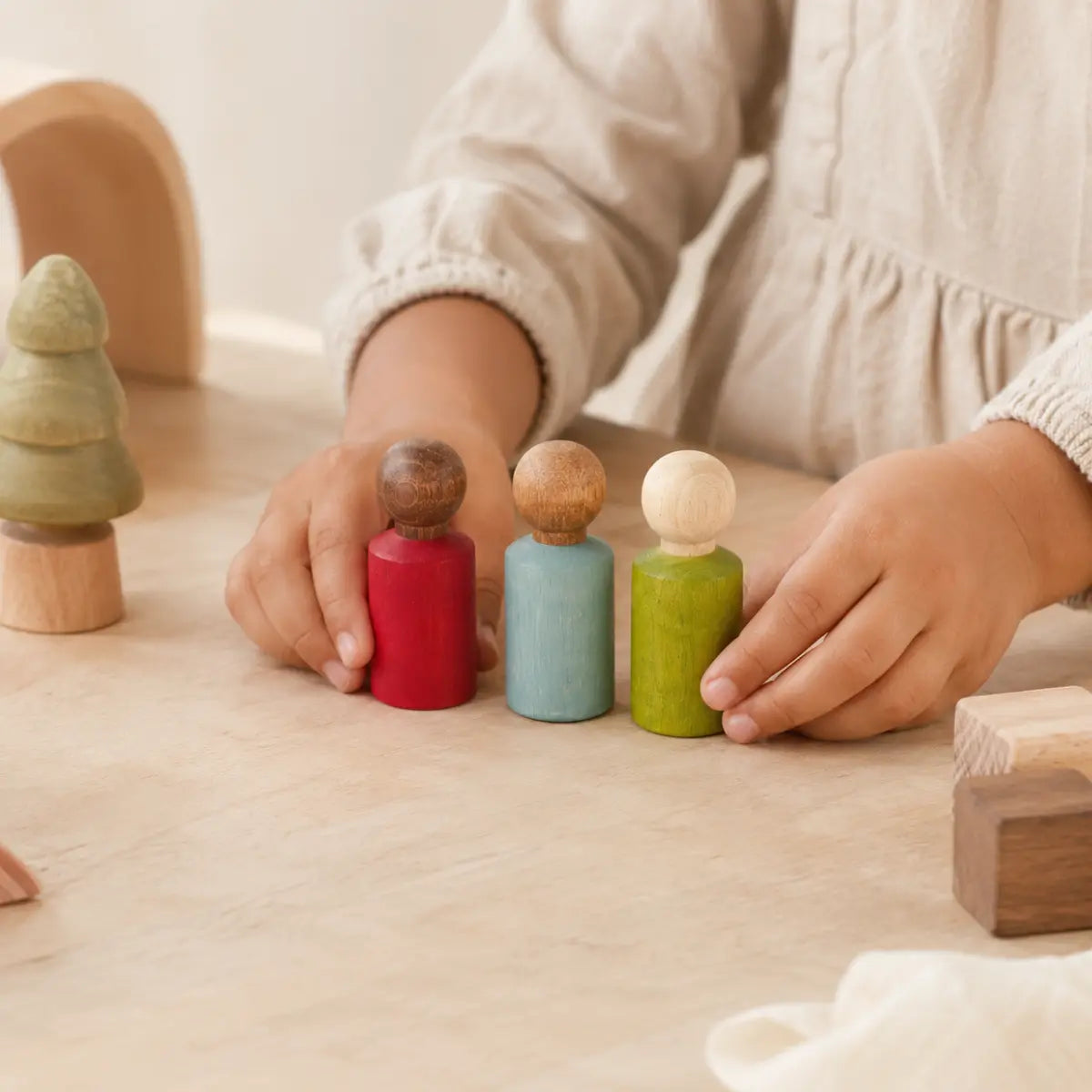 Child arranging three Lubulona wooden peg dolls in red, blue, and green for small world play