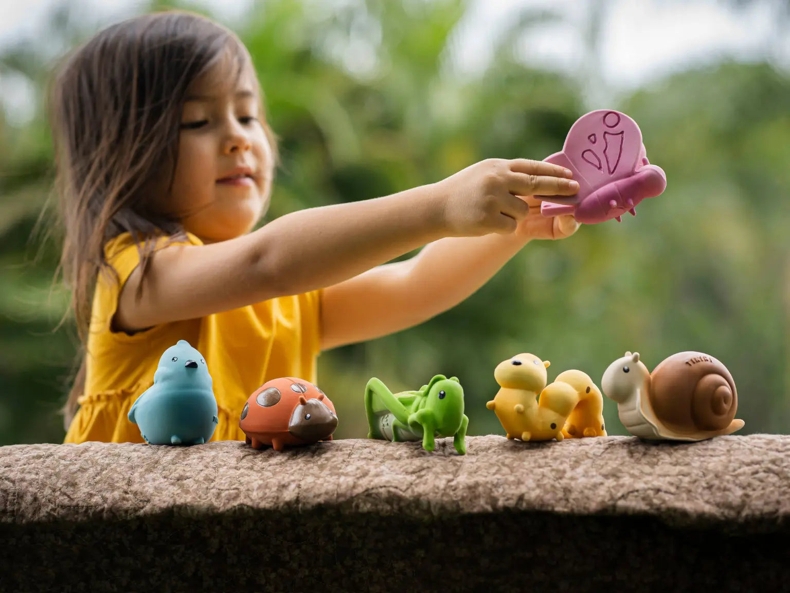 Child playing outdoors with natural rubber butterfly toy during sensory play