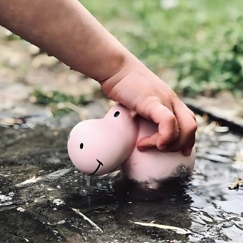 Child playing with natural rubber hippo toy in mud during outdoor sensory play