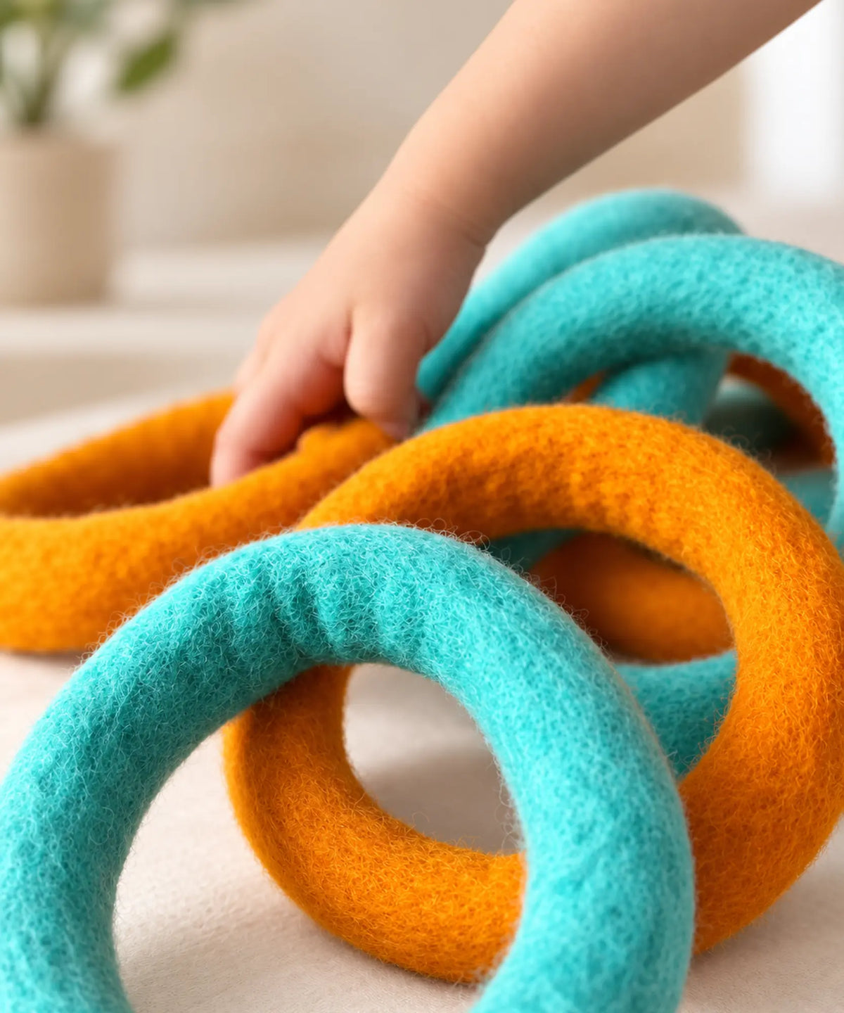 A child’s hand reaching into a pile of orange and teal wool felt rings.