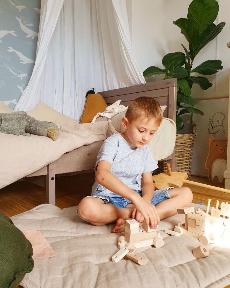Child playing with wooden train and stacking blocks in a natural playroom
