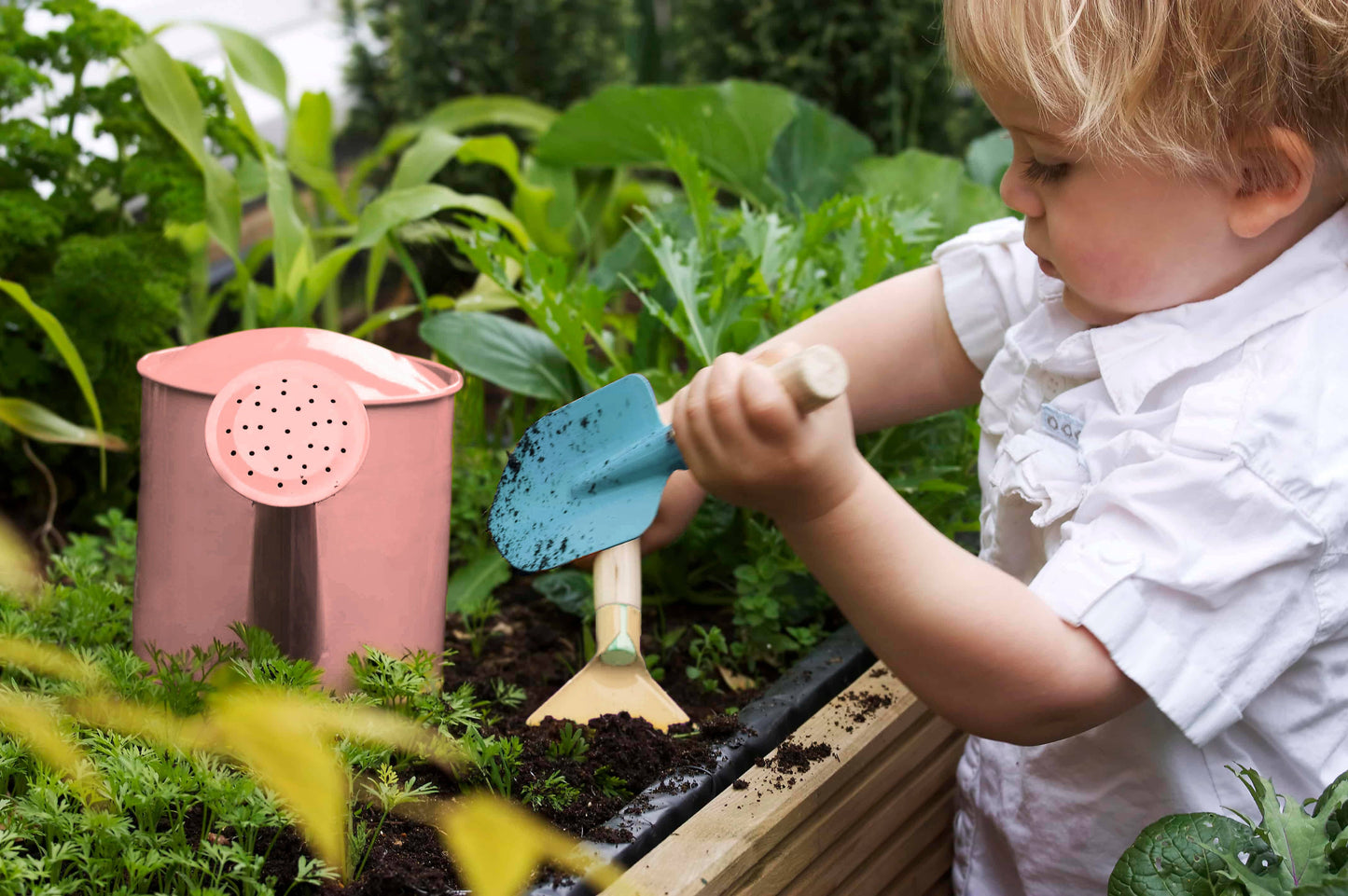 child using gardening tools and watering can in garden bed