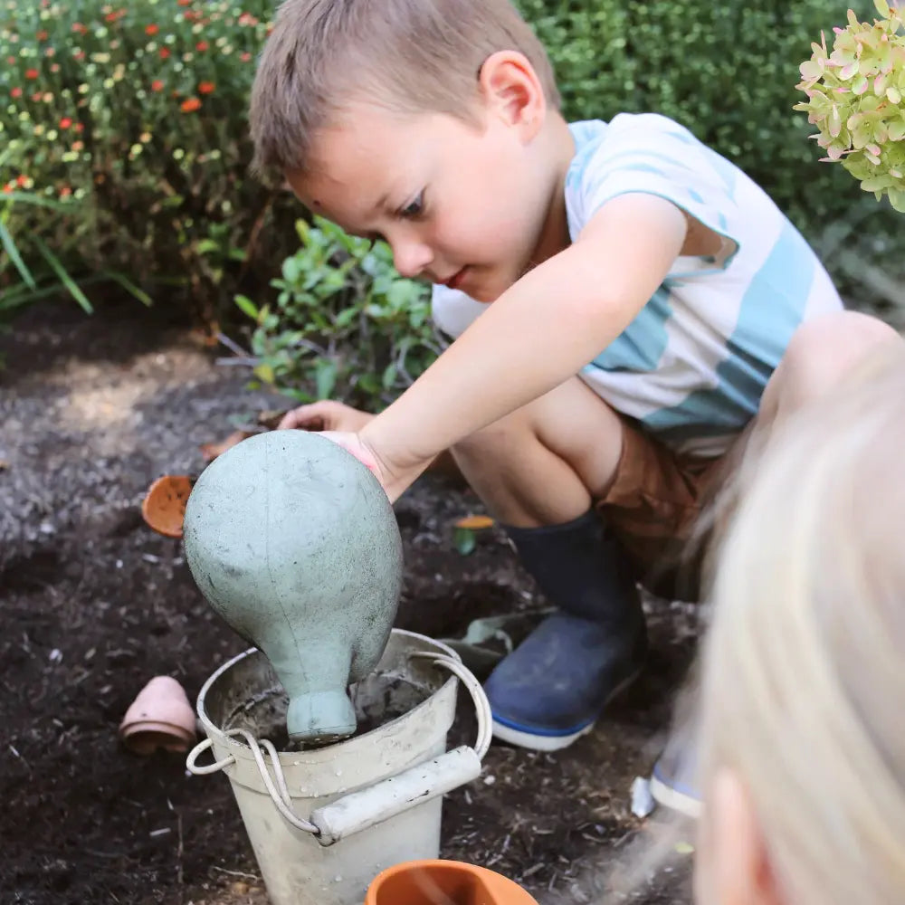 Child playing with a silicone gardening water can in a garden