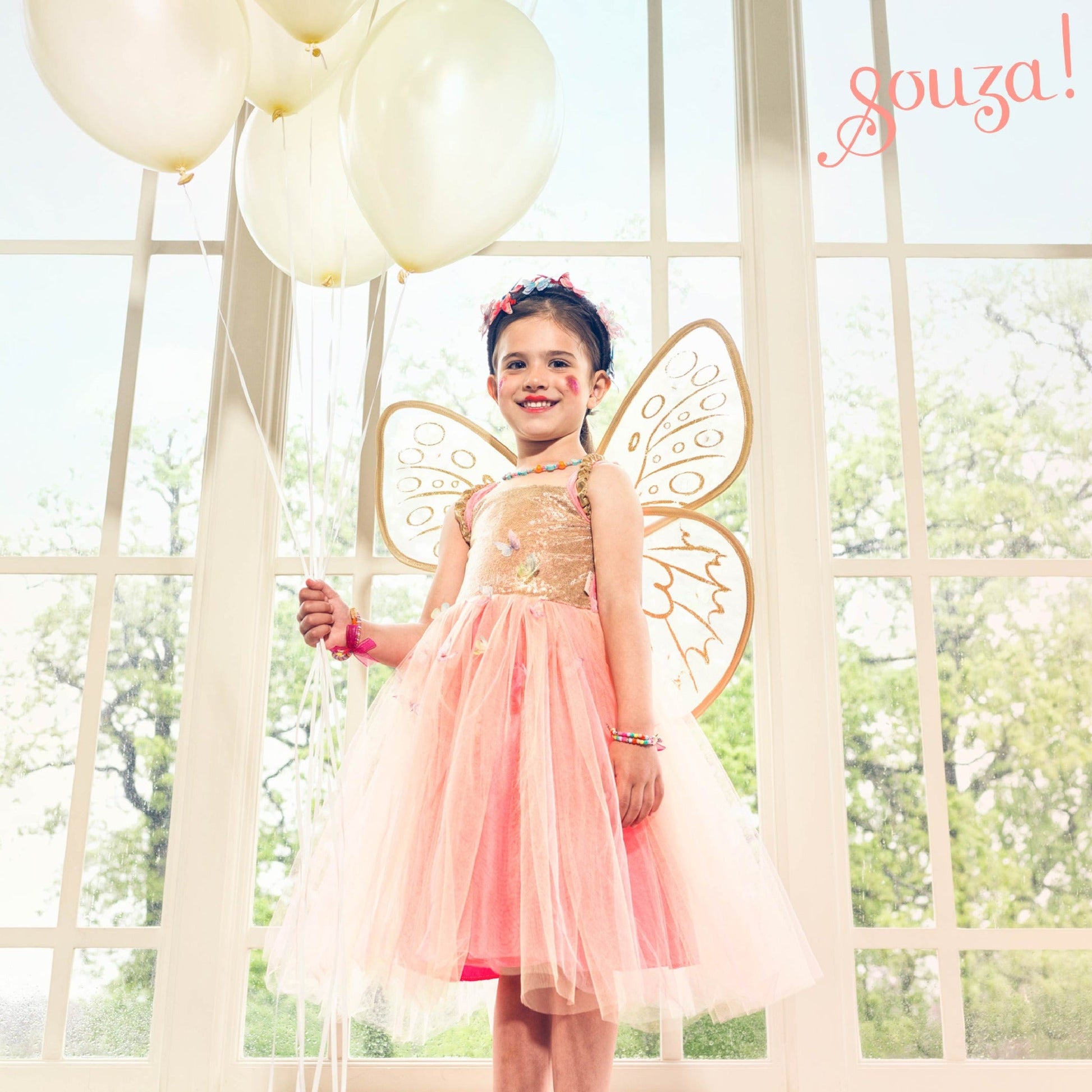 Child wearing fairy dress and wings set in apricot-orange and gold for imaginative play
