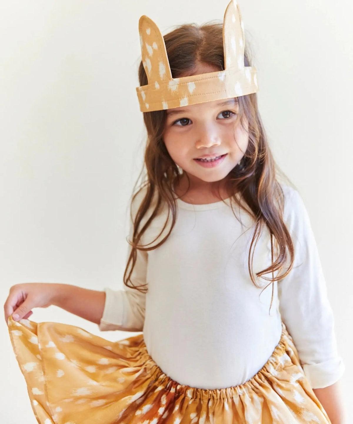 Child wearing fawn ears and holding up a matching fawn-print Playsilk
