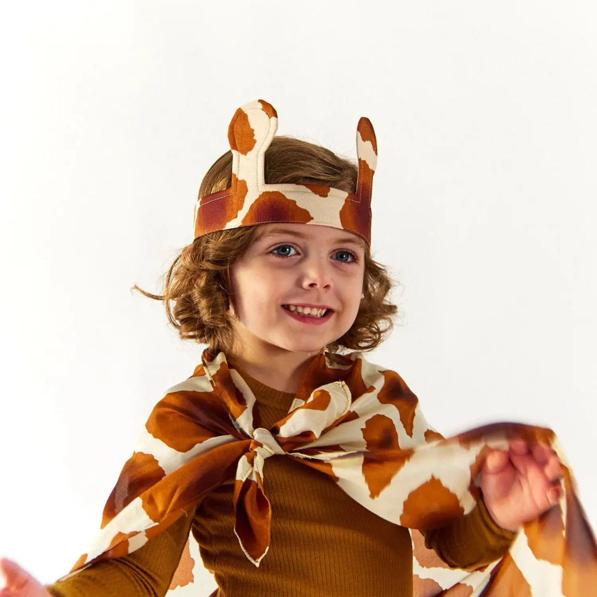 Smiling child wearing silk giraffe ears with a giraffe print playsilk tied as a cape for pretend play