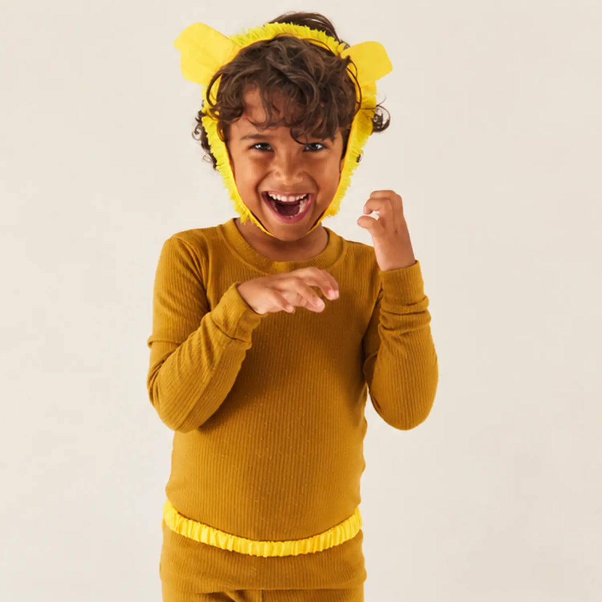Child wearing lion ears with a yellow mane, roaring with hands raised like claws during pretend play