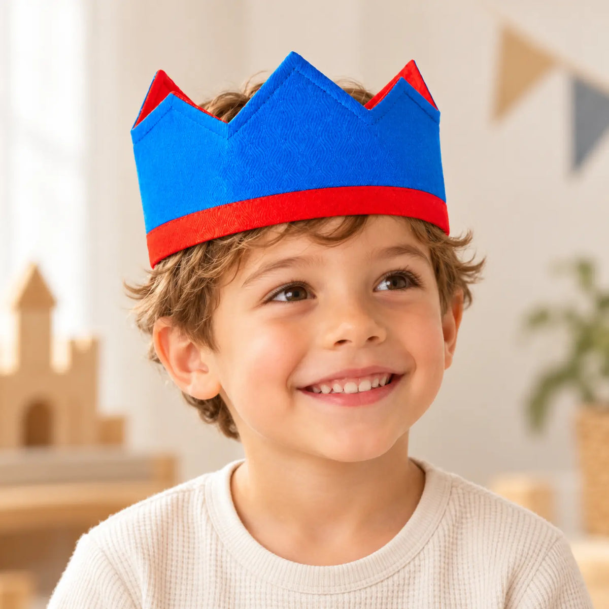 Smiling child wearing a royal blue and red silk crown for king, queen and knight pretend play