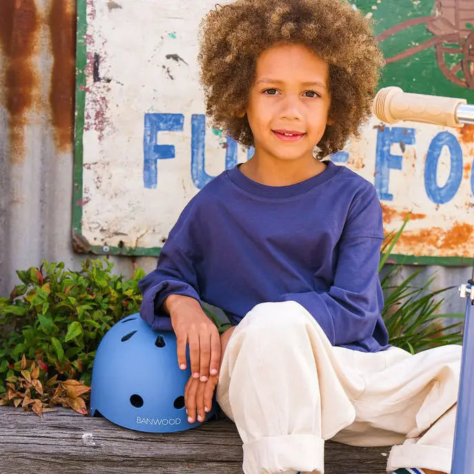 Child sitting next to a blue bike helmet with a rustic background