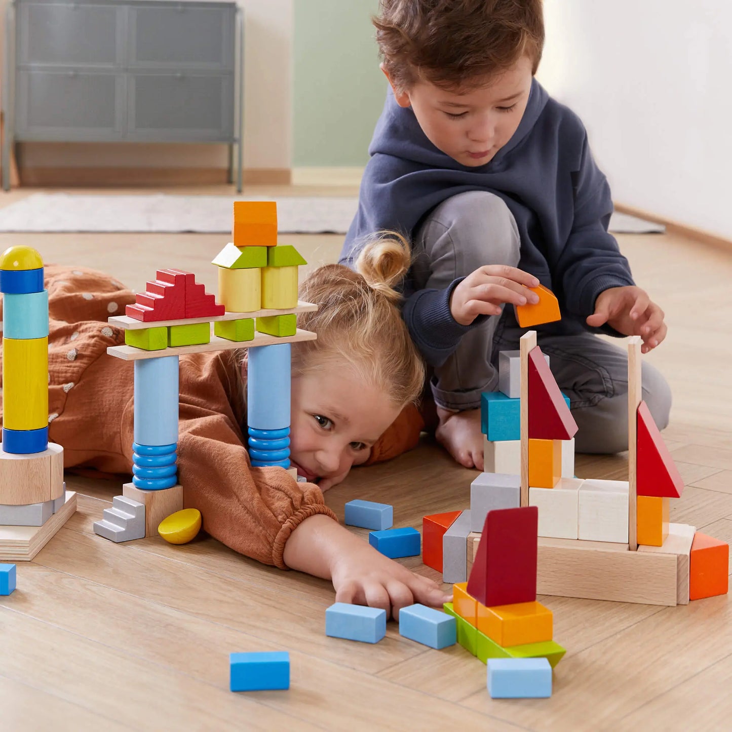 Two children playing with colorful building blocks on a wooden floor.