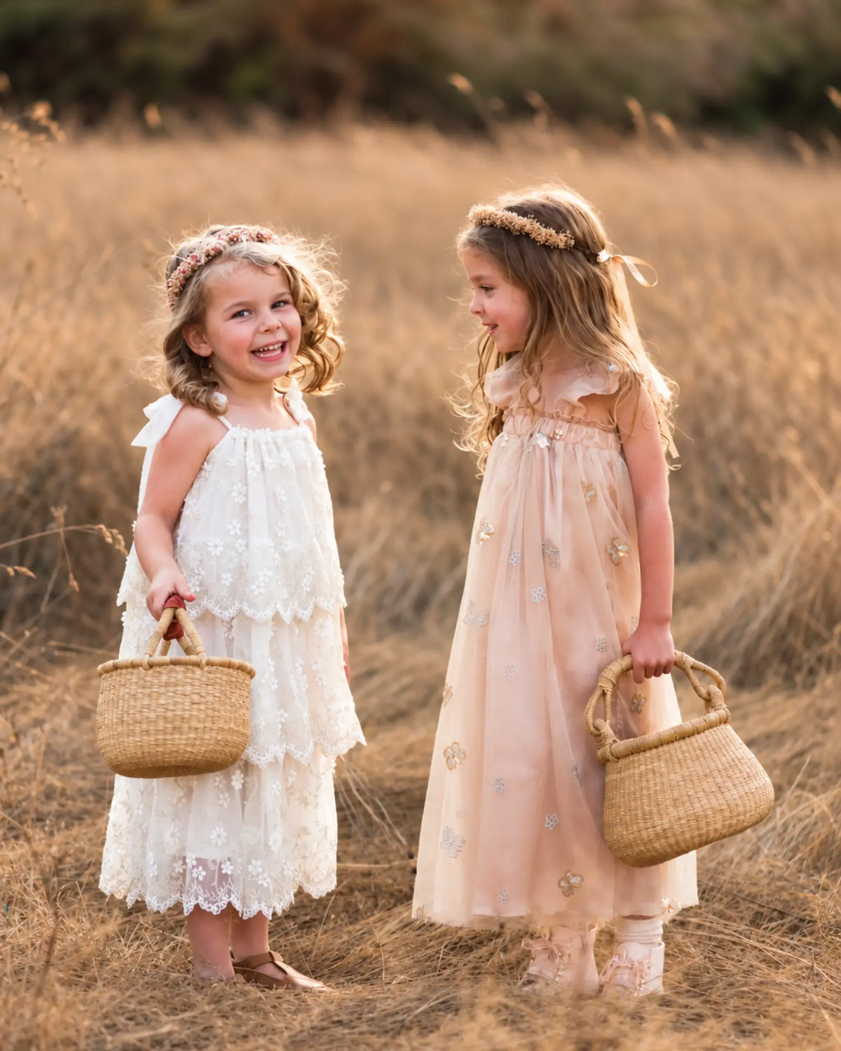 Two young girls carrying handwoven Bolga baskets while standing together in a sunlit meadow.