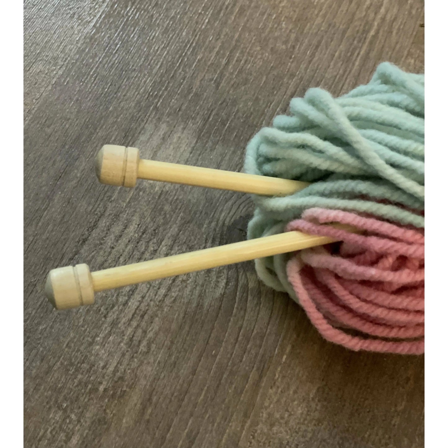 Prym Bamboo Single Point Knitting Needles in a pastel skein of yarn on wooden table