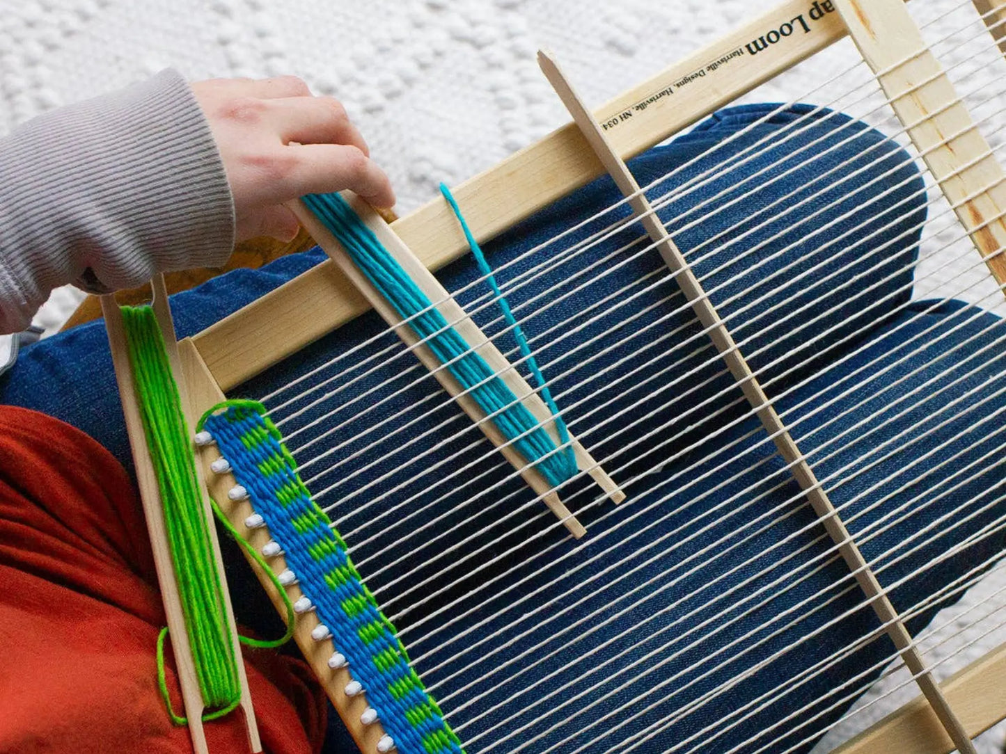 Person using a small wooden loom with blue and green yarn.