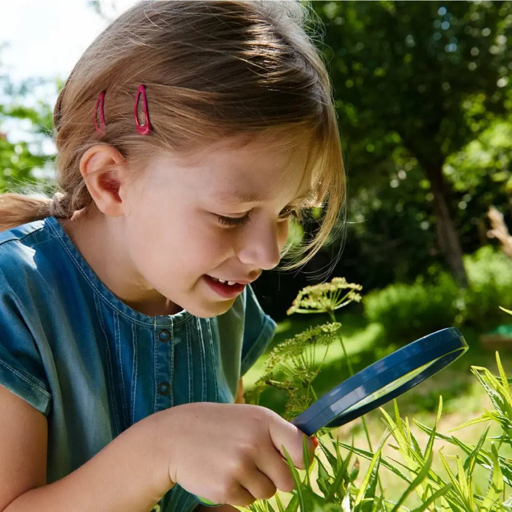 Child using a magnifying glass to examine plants outdoors