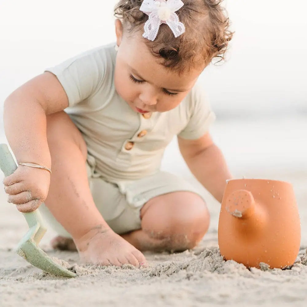 Child playing in the sand with a shovel and silicone garden set on a beach.