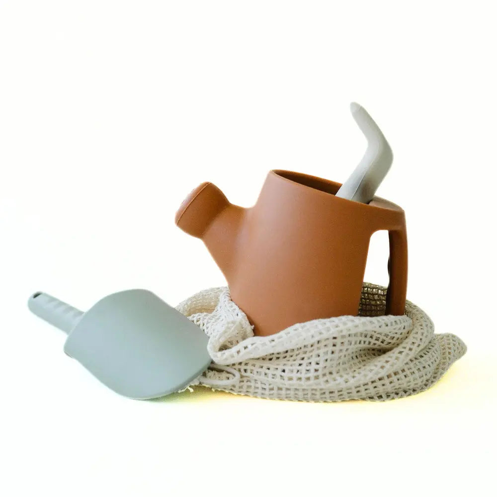 silicone children's watering can with a mesh bag and trowel on white background