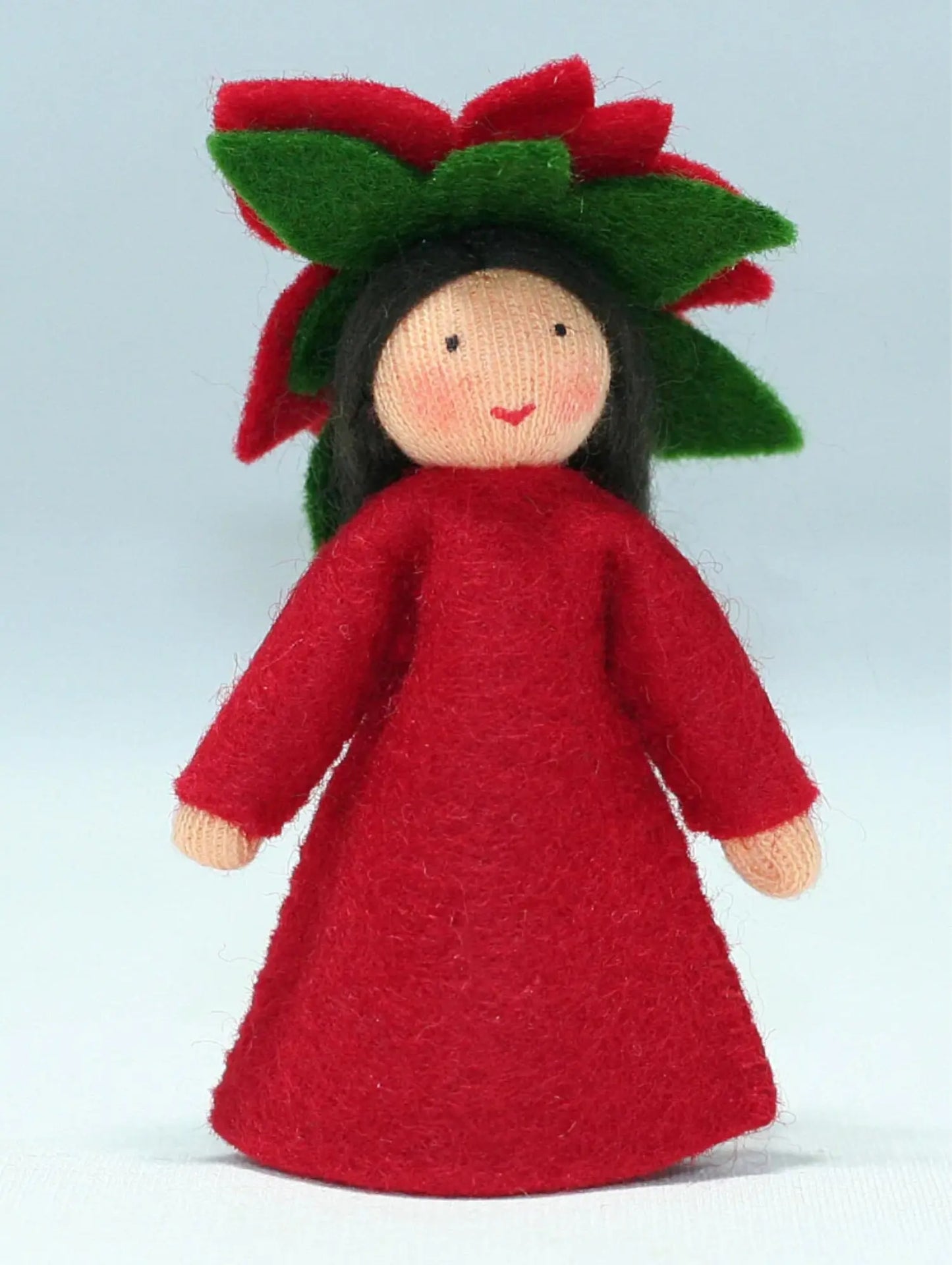Toy figure of a flower fairy in a red dress with green leaves on a light blue background