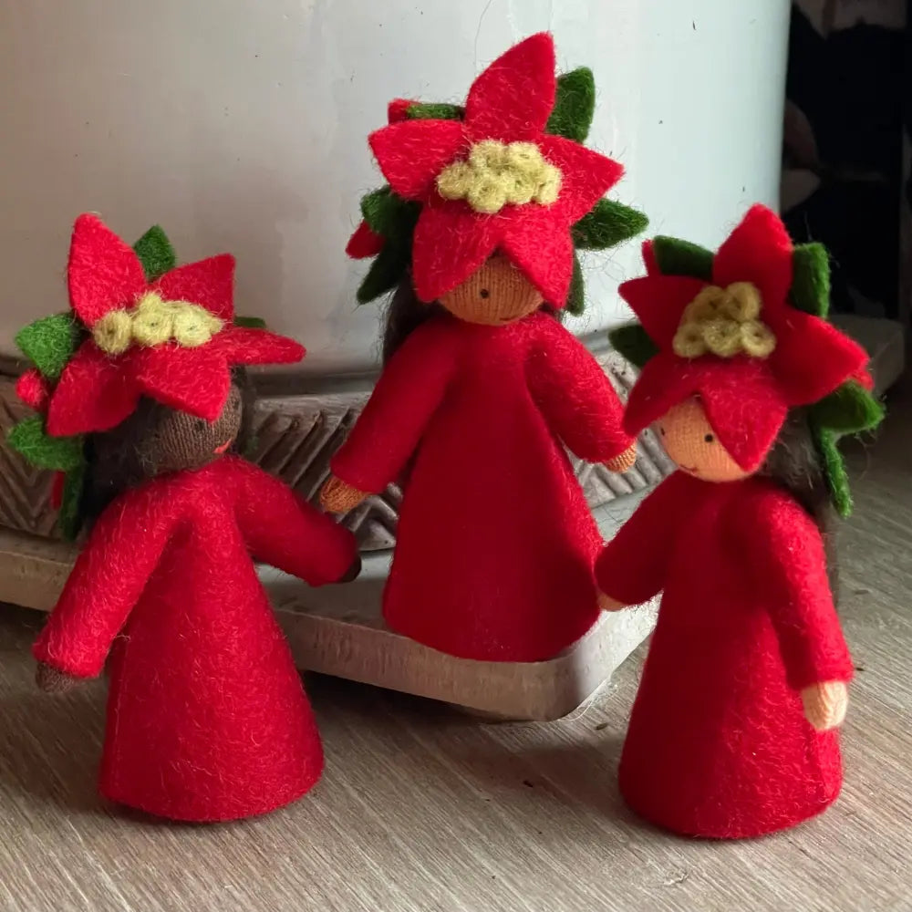 Three red dolls with flower-like heads on a wooden surface.