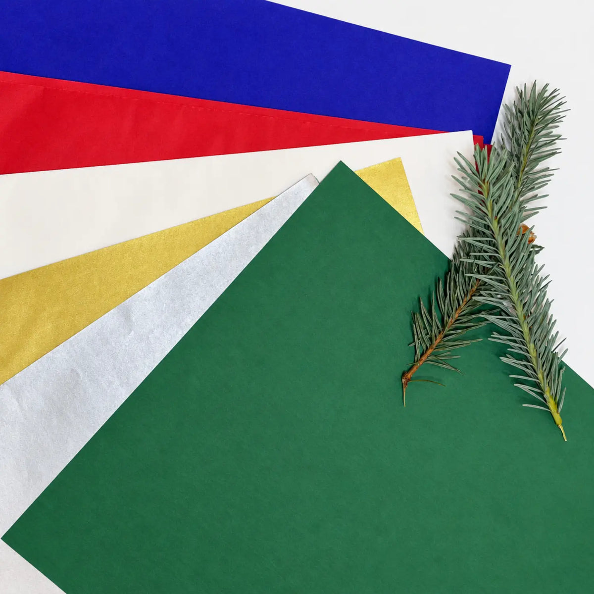 Red, green, white, and gold Japanese silk paper arranged with a small evergreen branch