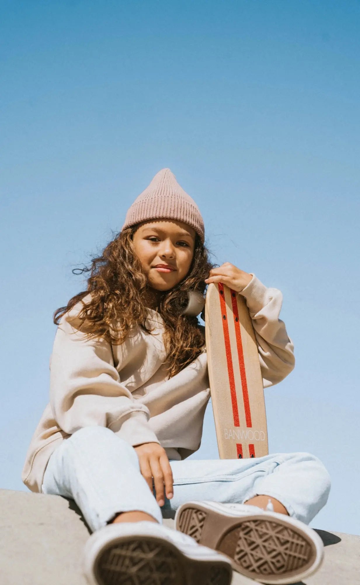 Person sitting on a ledge holding a skateboard against a clear blue sky
