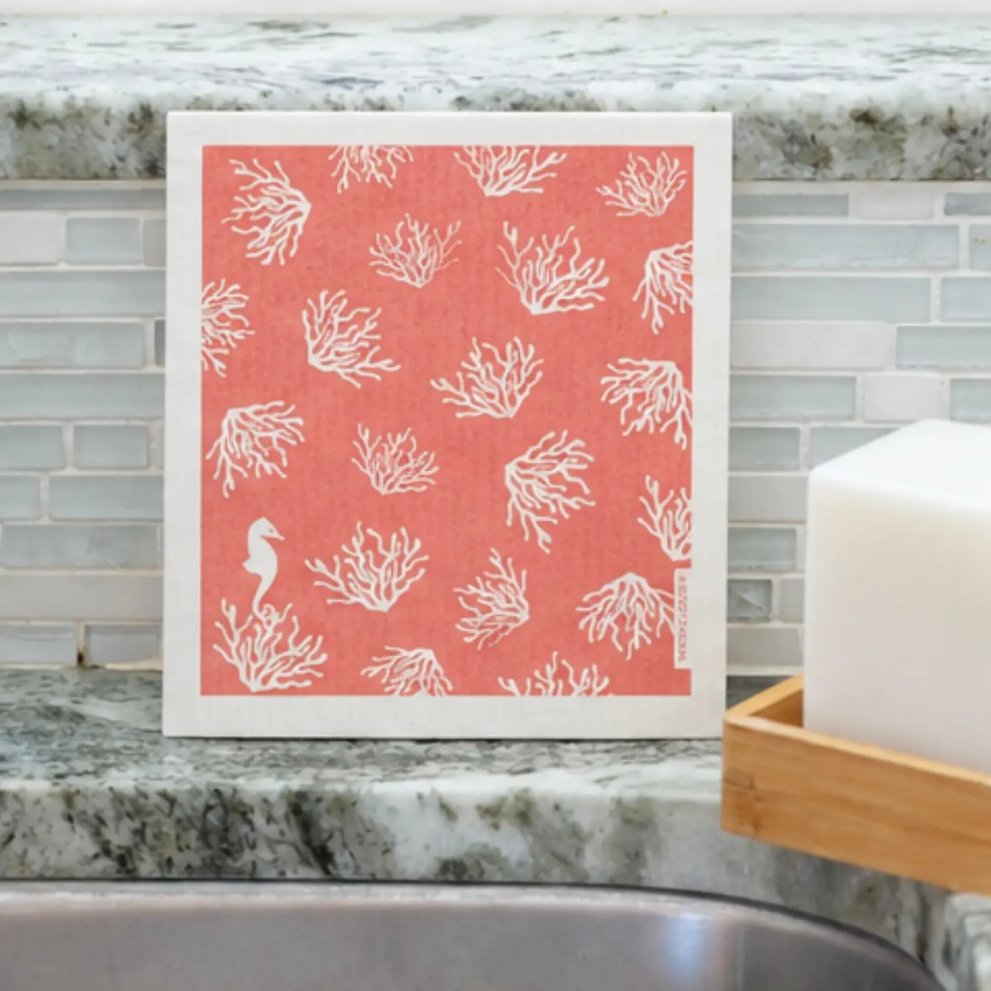 Coral Swedish dishcloth with white sea coral and seahorse design beside a kitchen sink