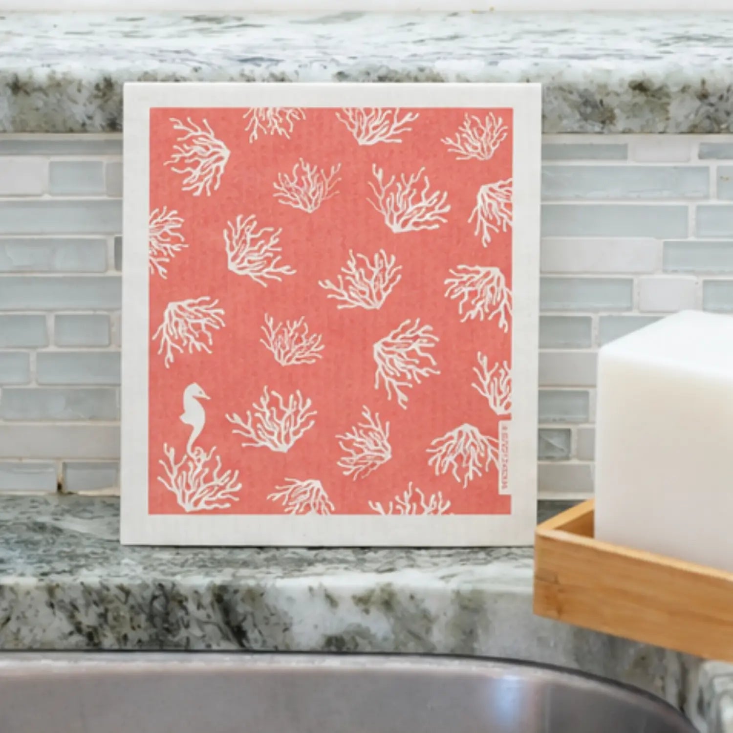 Coral Swedish dishcloth with white sea coral and seahorse design beside a kitchen sink