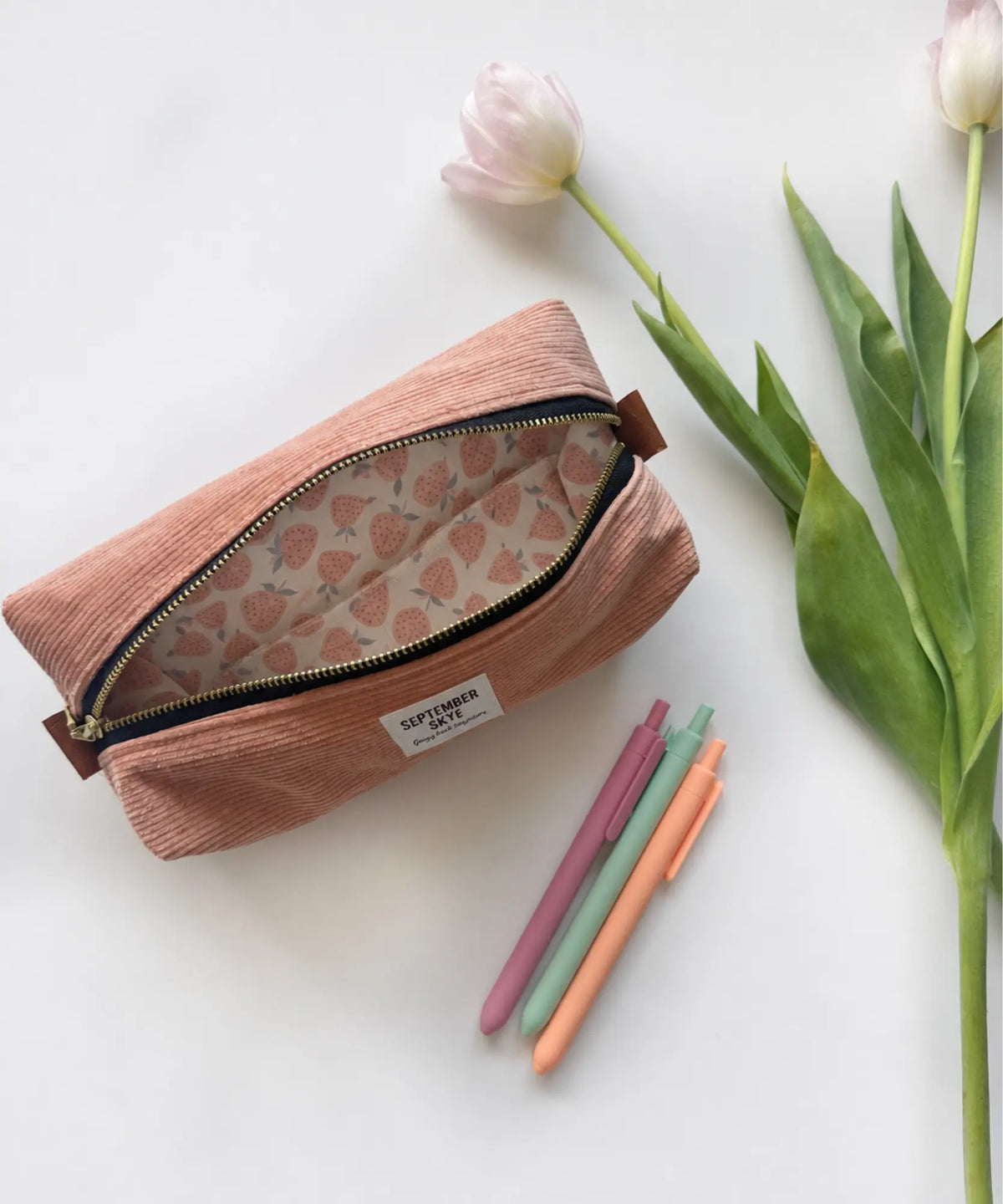 An open dusty pink corduroy pencil pouch bag with a strawberry patterned lining