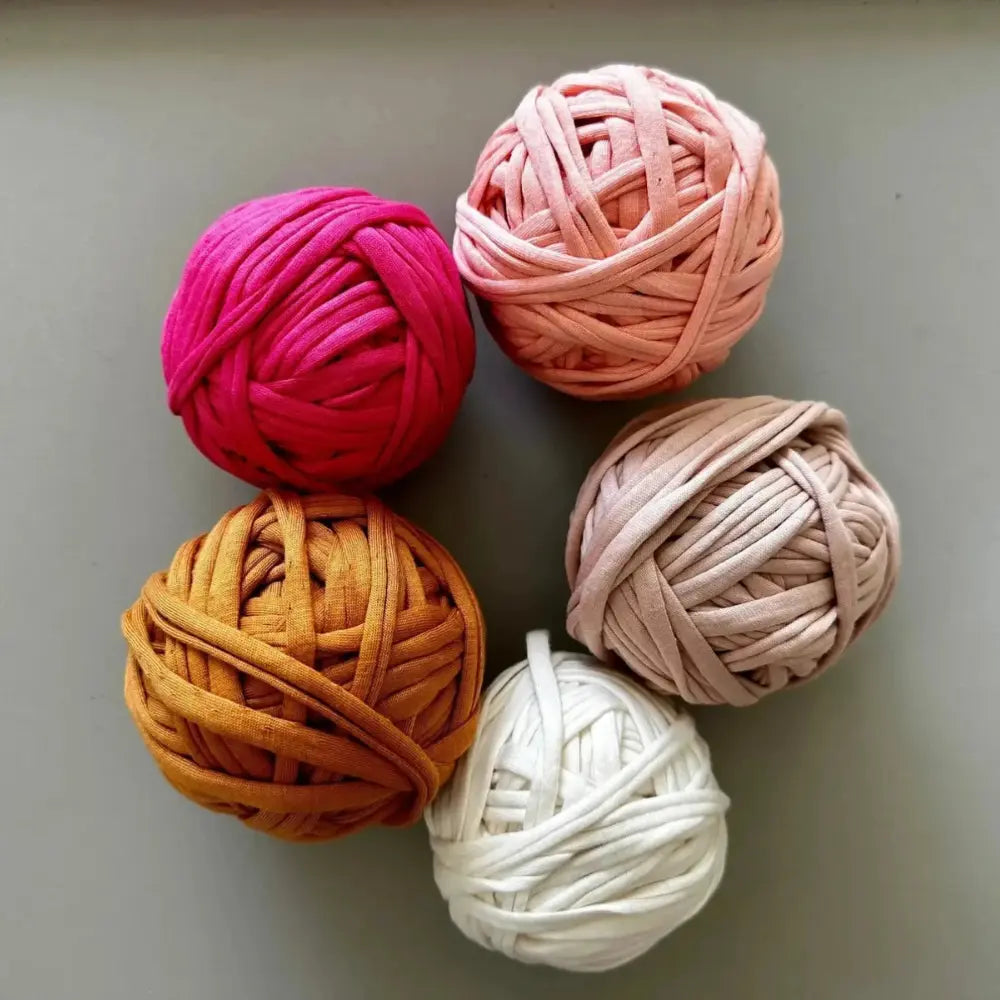 Five balls of potholder yarn in pink, orange, white, and peach on a gray background