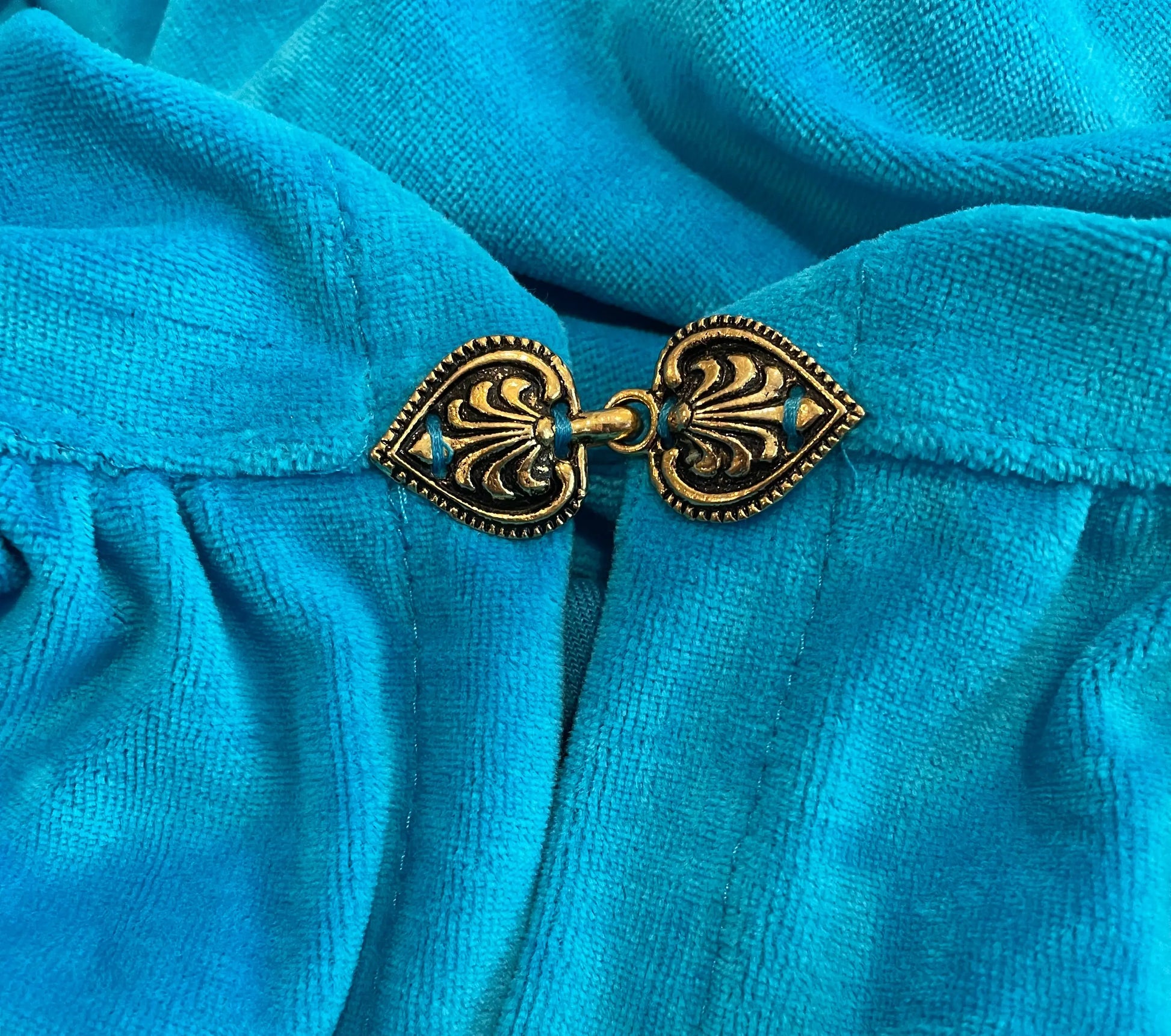 Close-up of decorative metal clasp on blue cotton velour hooded cape