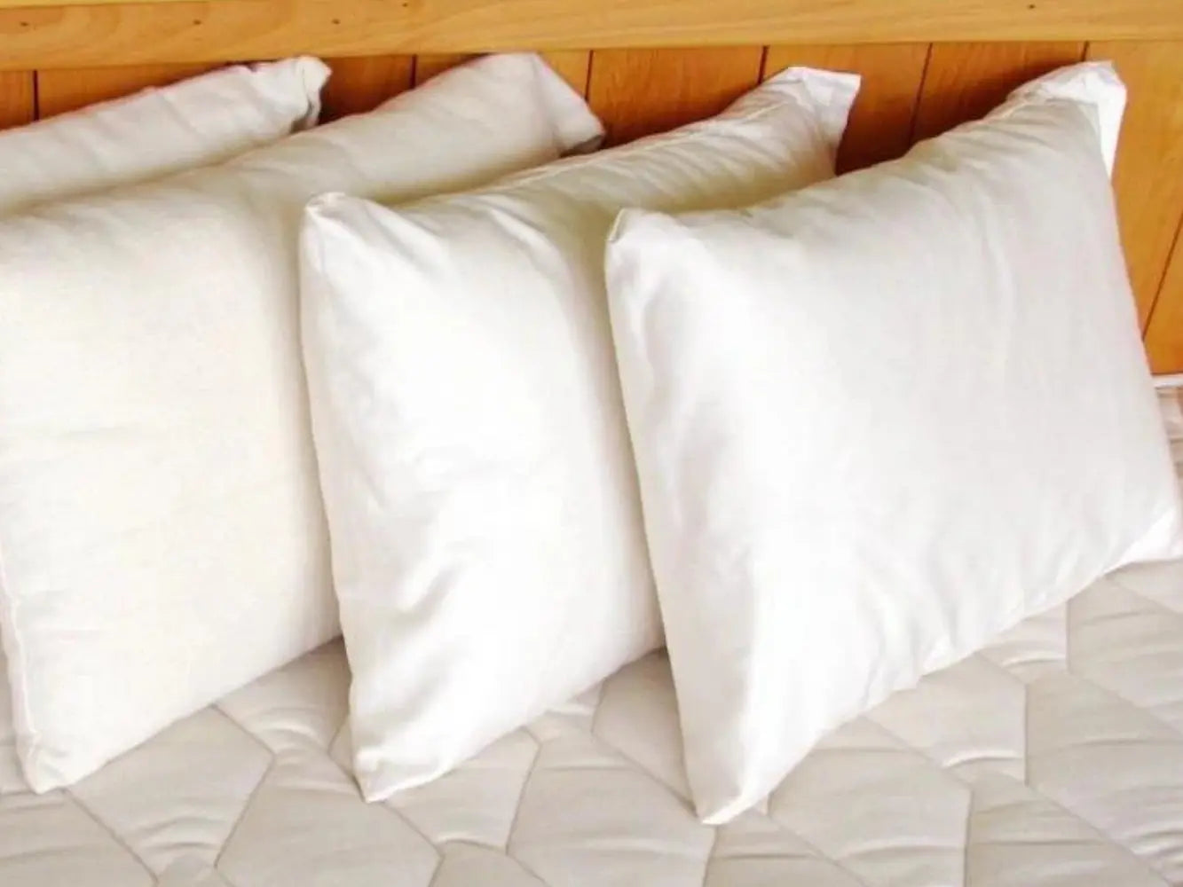 White cotton and wool pillows on a bed with a wooden headboard
