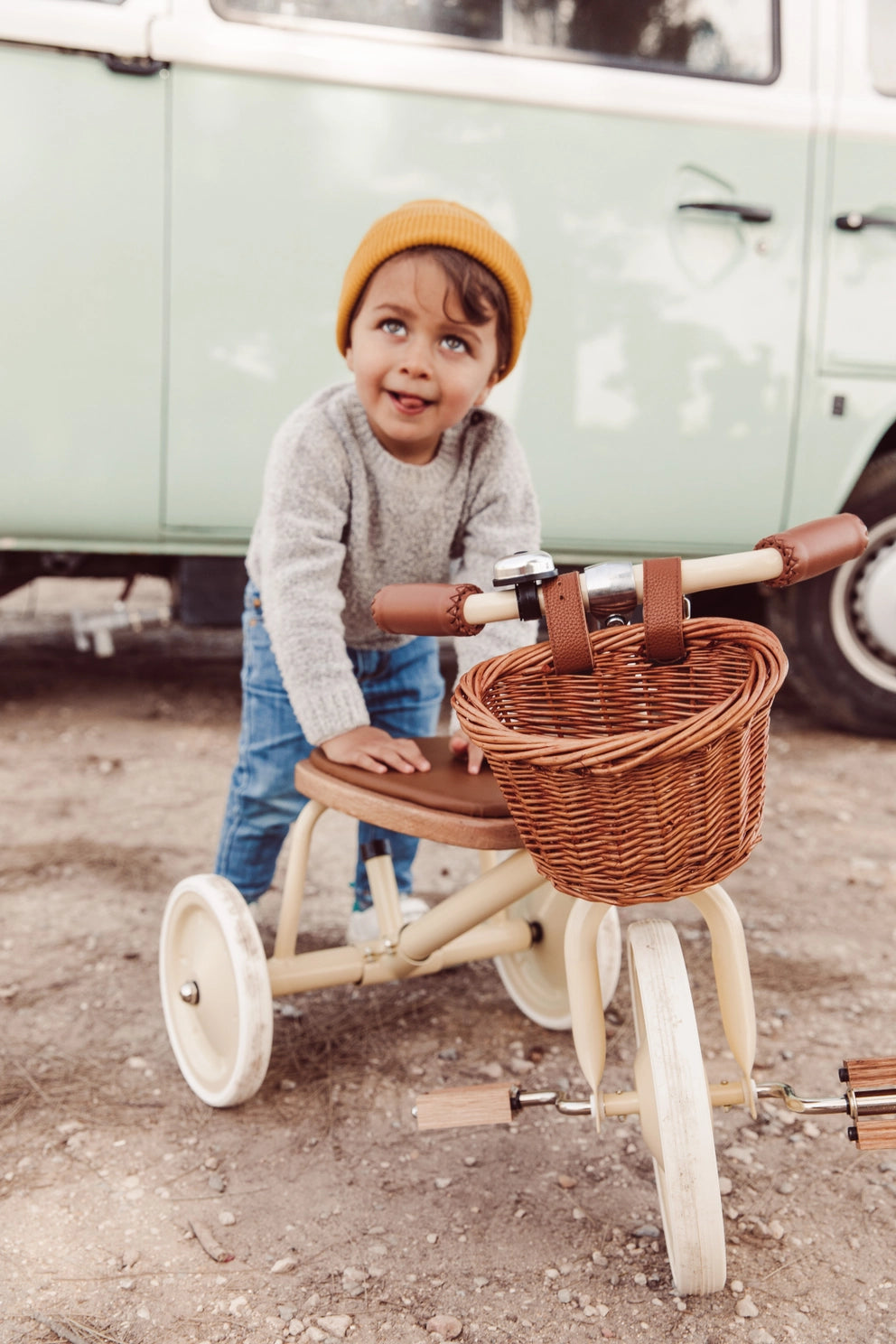 Child riding a tricycle with a basket in front of a vintage van.
