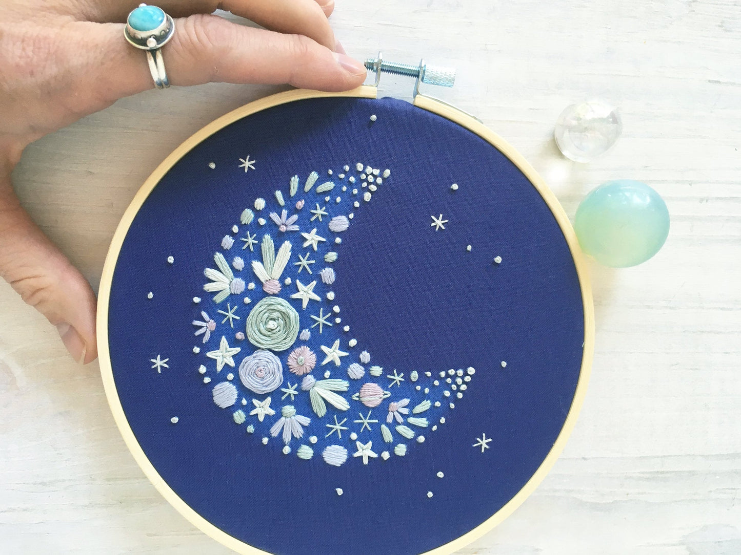 Embroidery hoop with floral crescent moon design on a blue background
