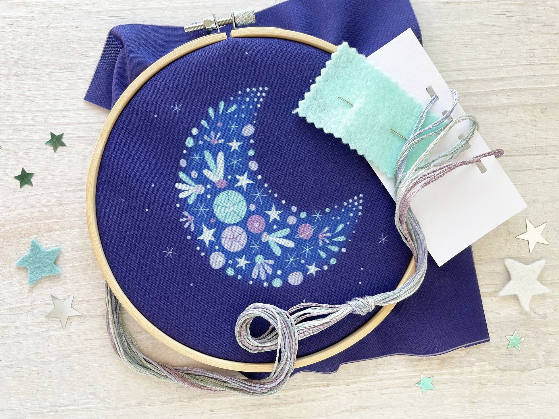 Embroidery hoop with floral crescent moon design and contents on a blue fabric background