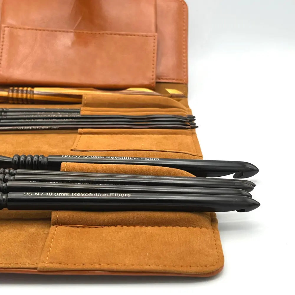 Set of archery arrows with black tips and labels on a brown leather case.