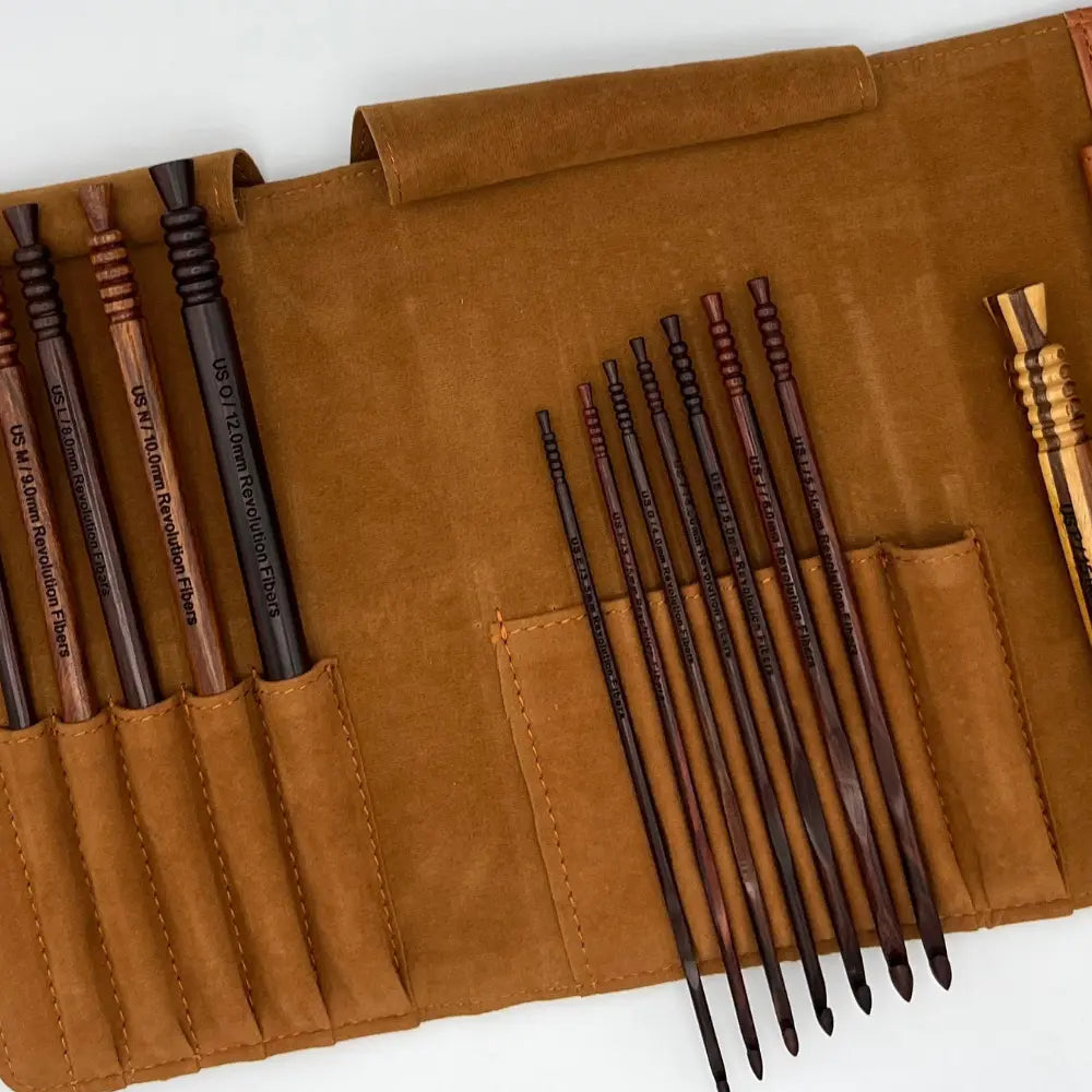 Set of wooden knitting needles in a brown leather case on a white background