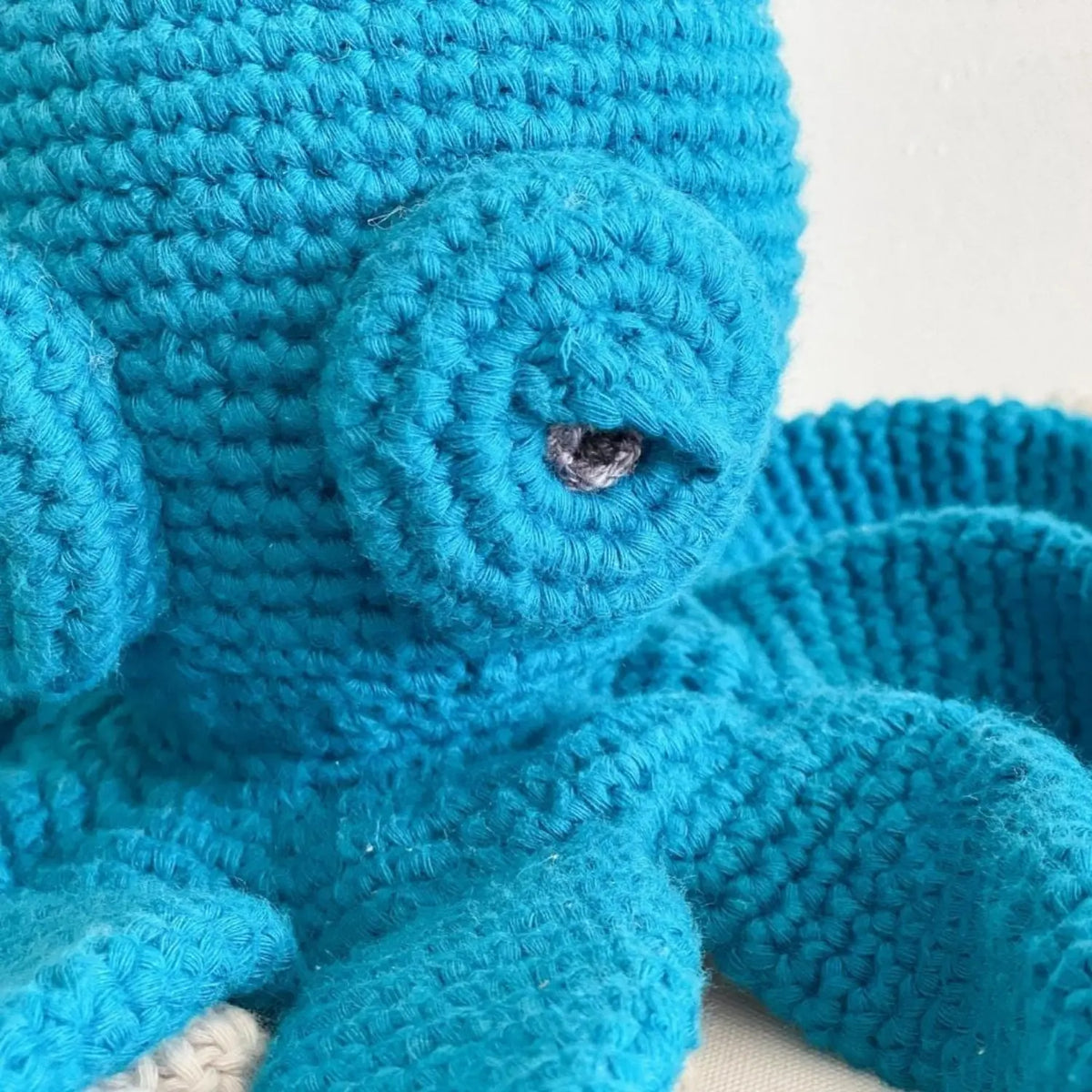 Close-up of the lagoon teal crochet octopus's spiral eye and hand-crocheted organic cotton stitches