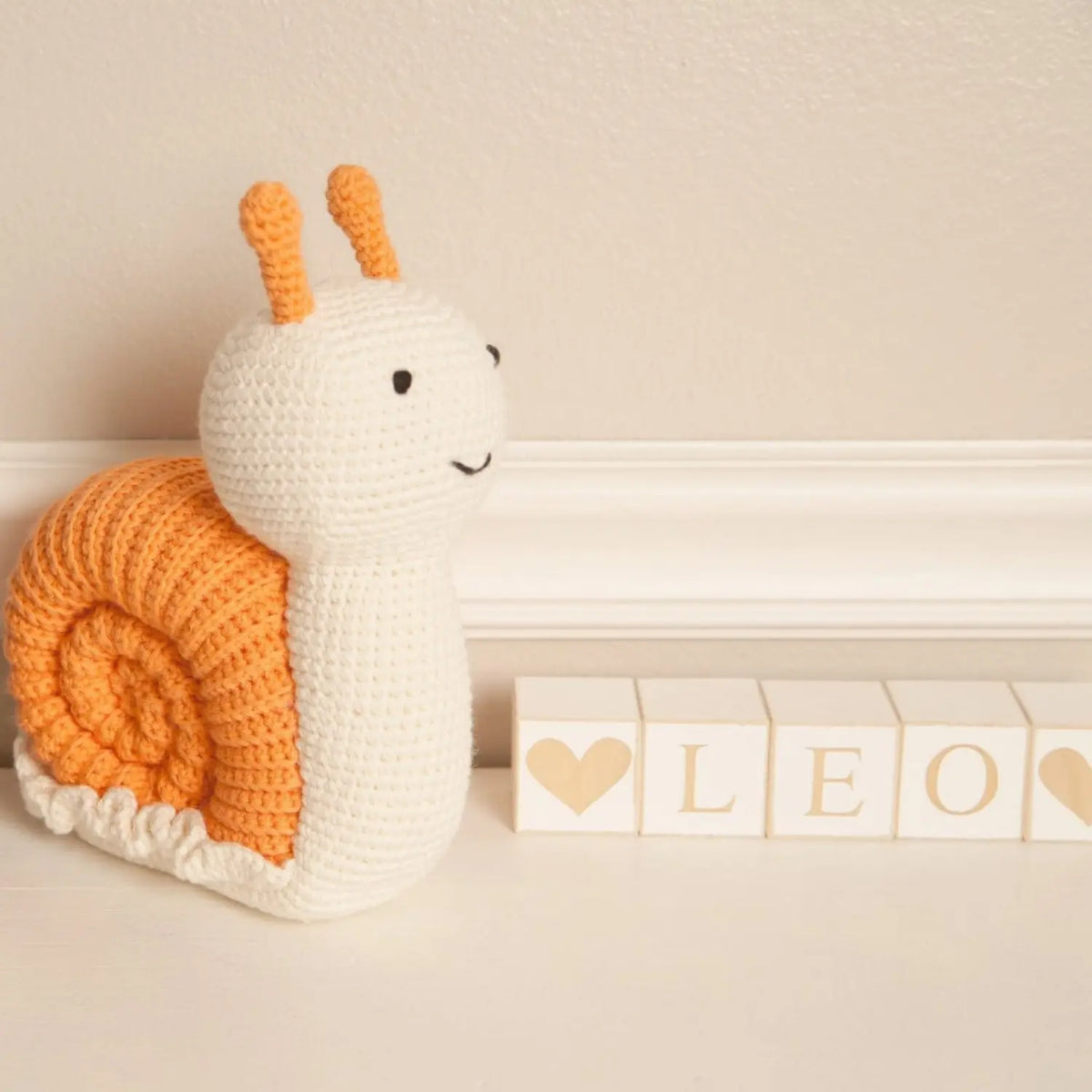 Handmade crochet snail stuffed animal on a nursery shelf beside wooden letter blocks