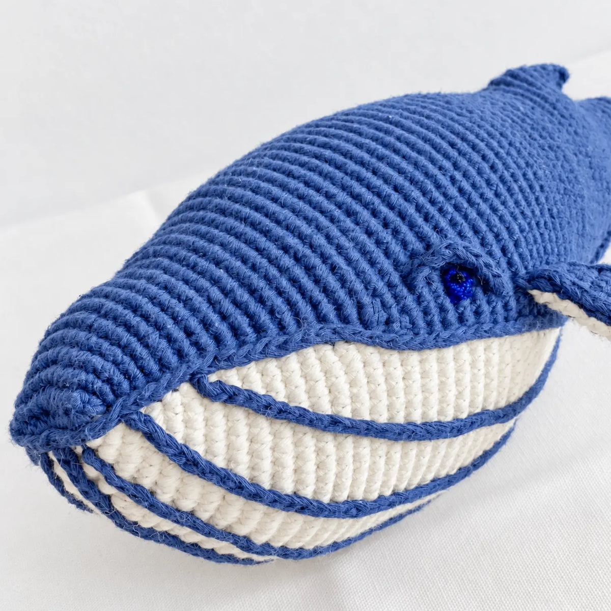 Close-up of the deep blue crochet whale's face showing its blue eye, cream striped belly and hand-crocheted cotton stitches