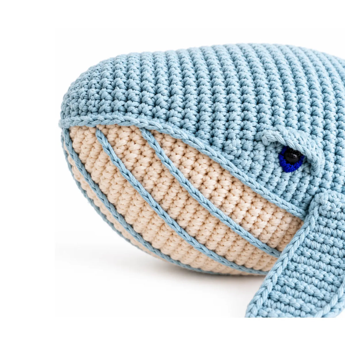 Close-up of the misty blue crochet whale's face showing its dark blue eye, cream striped belly and hand-crocheted cotton stitches