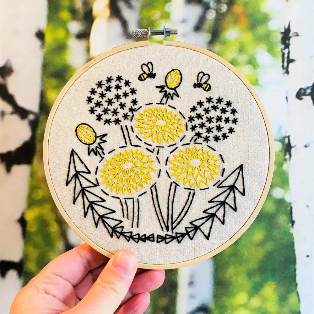 Beginner dandelion embroidery hoop with bees held outdoors in natural light