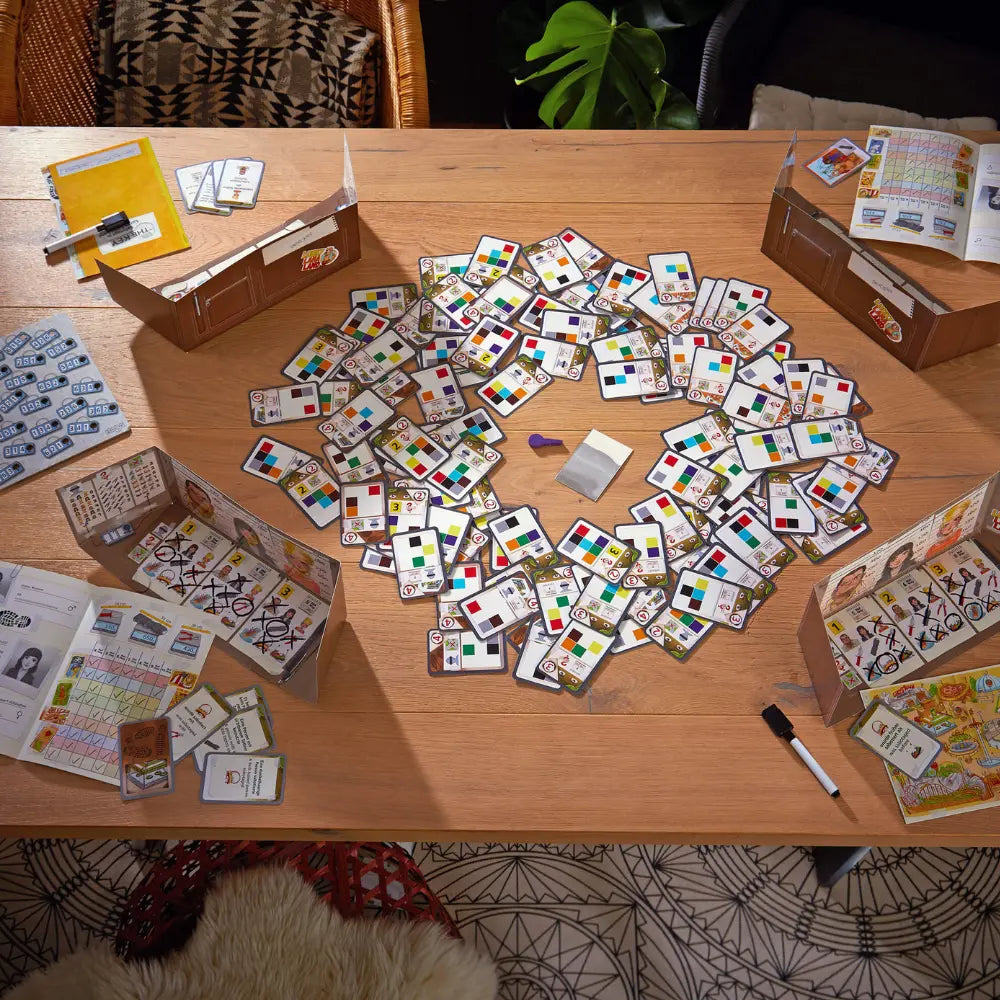 Scattered board game components on a wooden table with boxes and cards.