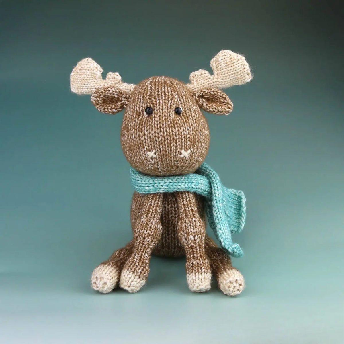 Finished Maddie Moose hand-knit toy seated with cream hooves, antlers, and blue scarf