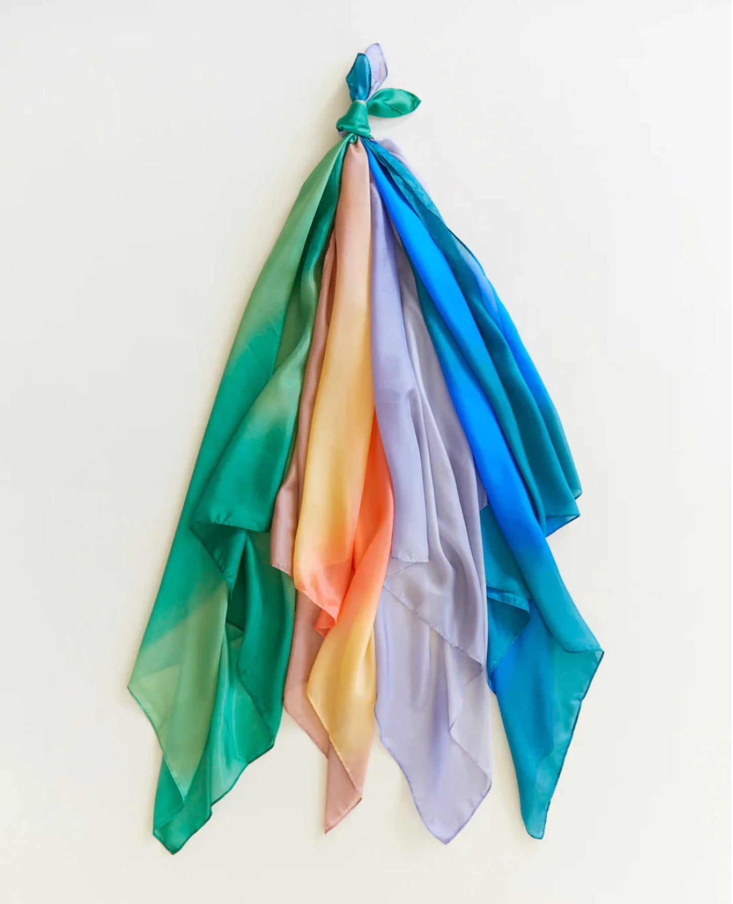 Earth playsilks in forest desert, stone, and ocean tied together into a bundle on a light background