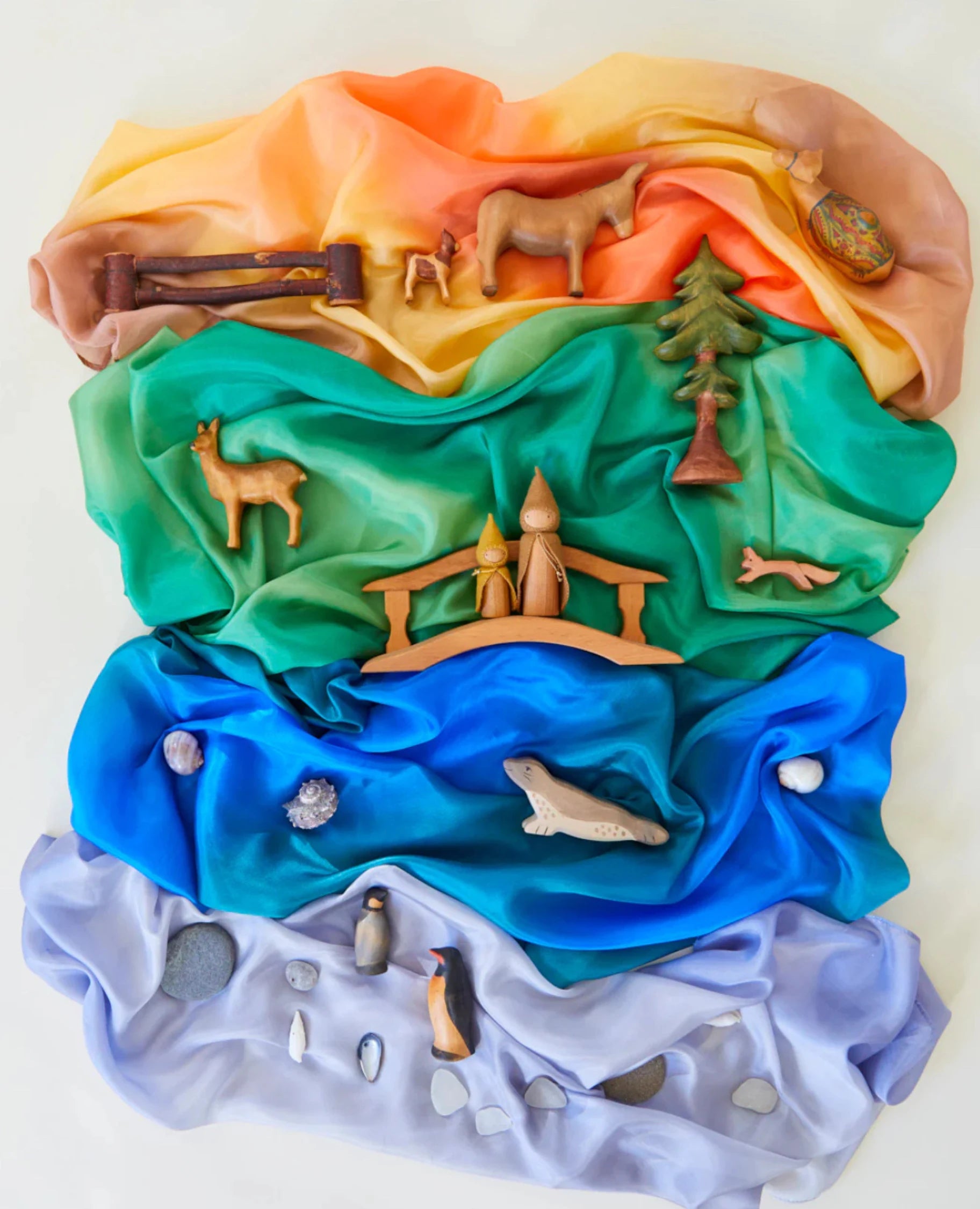Four Earth playsilks in desert, forest, ocean, and stone with wooden toys, shells, and stones on top